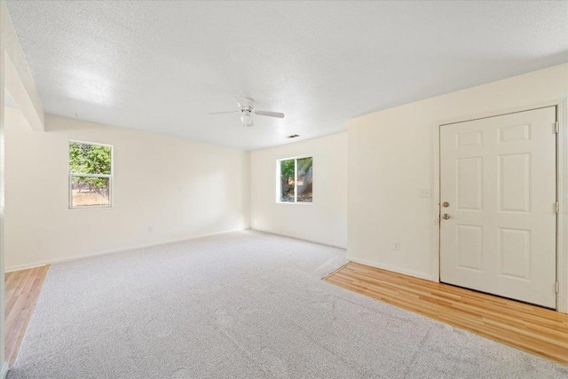 unfurnished room with a textured ceiling, ceiling fan, and light colored carpet