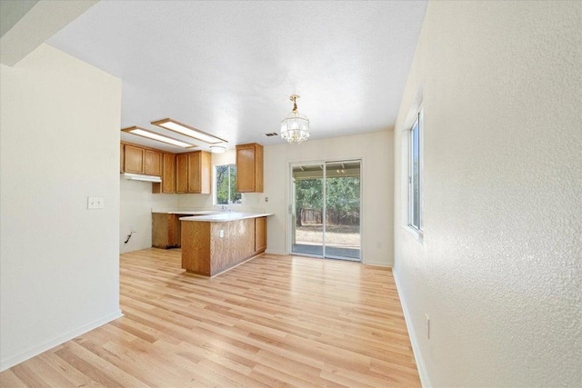 kitchen with decorative light fixtures, light hardwood / wood-style flooring, kitchen peninsula, and a chandelier