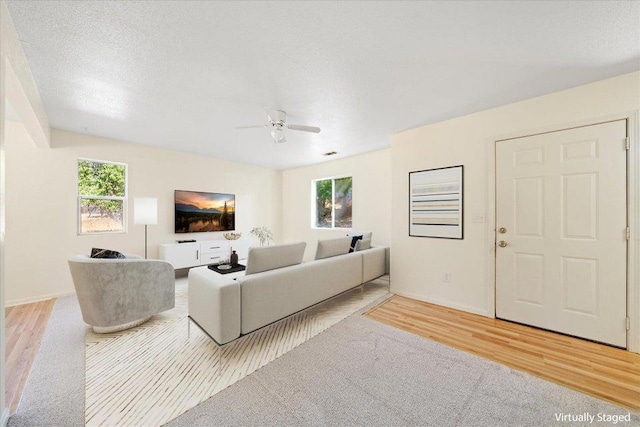 living room with ceiling fan, a textured ceiling, and light hardwood / wood-style floors