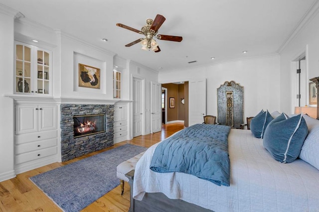 bedroom featuring a fireplace, ceiling fan, light hardwood / wood-style flooring, and crown molding