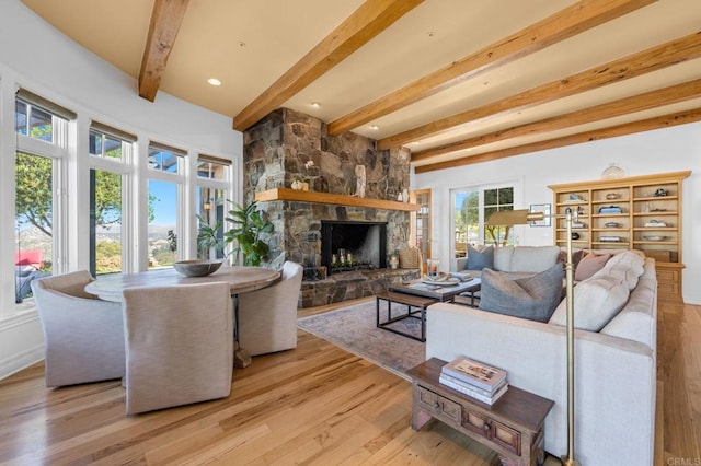 living room with a stone fireplace, light hardwood / wood-style flooring, and beamed ceiling