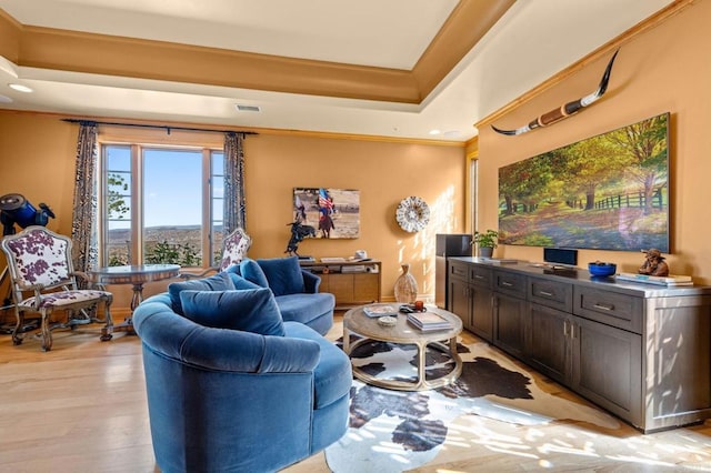 living room featuring ornamental molding, light hardwood / wood-style floors, and a tray ceiling