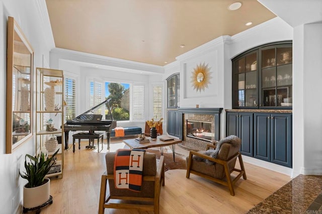 sitting room with light wood-type flooring, crown molding, and a premium fireplace