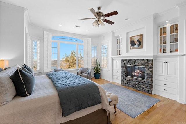 bedroom featuring a stone fireplace, ceiling fan, light hardwood / wood-style floors, and ornamental molding