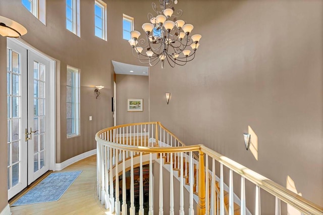 interior space with french doors, a healthy amount of sunlight, an inviting chandelier, a towering ceiling, and light hardwood / wood-style floors