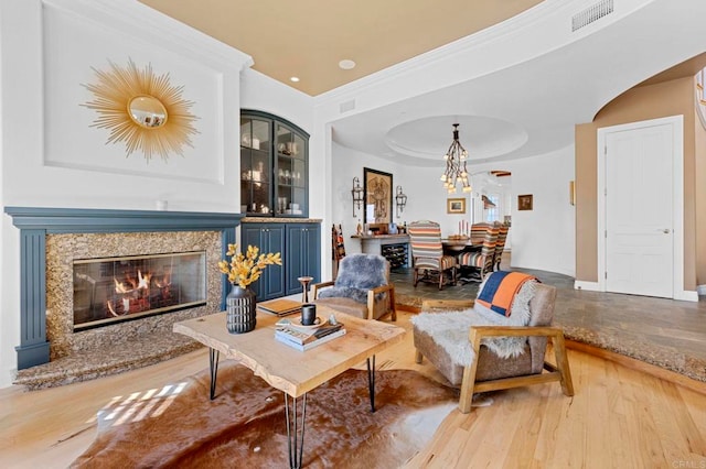 living room with an inviting chandelier, a raised ceiling, crown molding, light hardwood / wood-style flooring, and a premium fireplace