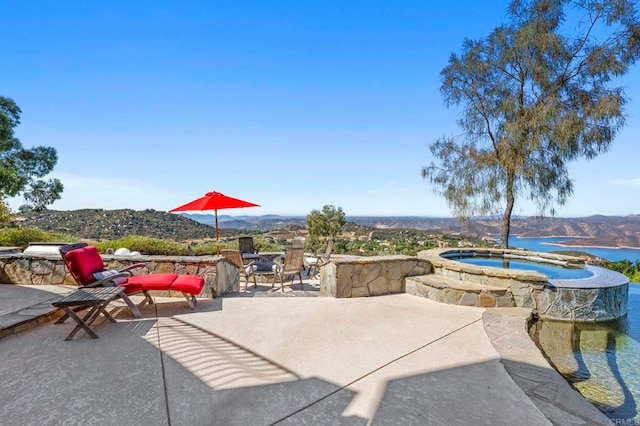 view of patio / terrace with an in ground hot tub, a water view, and a fire pit