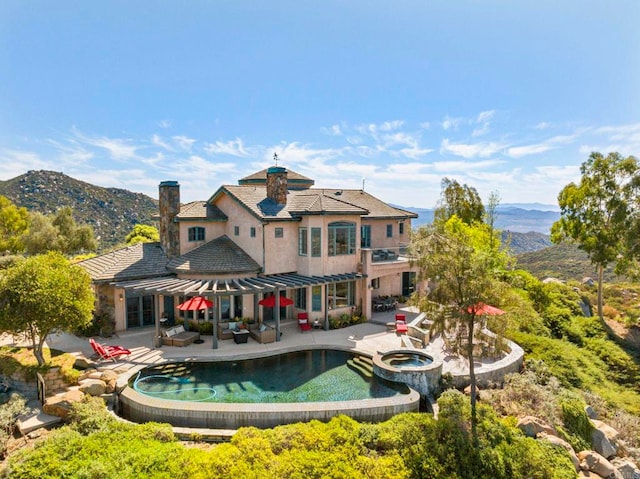 back of house featuring outdoor lounge area, a mountain view, a balcony, a patio area, and an in ground hot tub