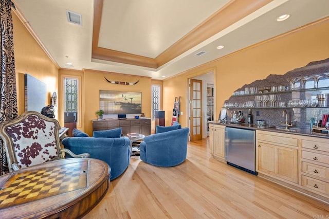 living room featuring a raised ceiling, light wood-type flooring, wet bar, and crown molding