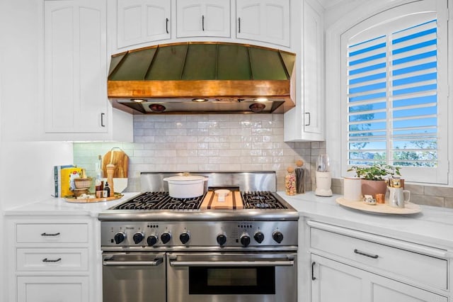 kitchen featuring premium range hood, decorative backsplash, white cabinets, and stainless steel range oven