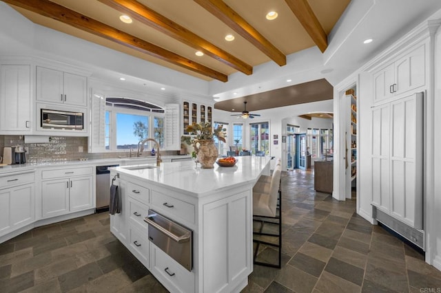 kitchen featuring tasteful backsplash, white cabinetry, stainless steel appliances, and an island with sink