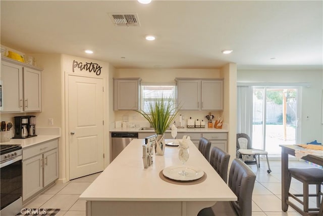 kitchen with gray cabinetry, a center island, stainless steel appliances, a breakfast bar area, and light tile patterned floors