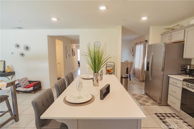 kitchen with a breakfast bar, light tile patterned flooring, an island with sink, and appliances with stainless steel finishes