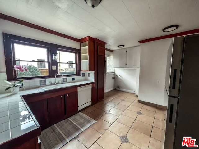 kitchen with sink, light tile patterned flooring, dishwasher, tile countertops, and stainless steel refrigerator