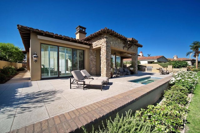 rear view of house with an in ground hot tub, a patio area, and exterior kitchen