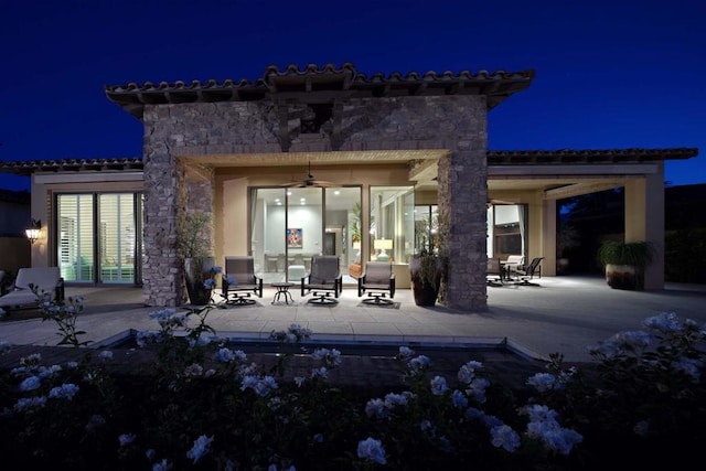 back house at night with ceiling fan and a patio