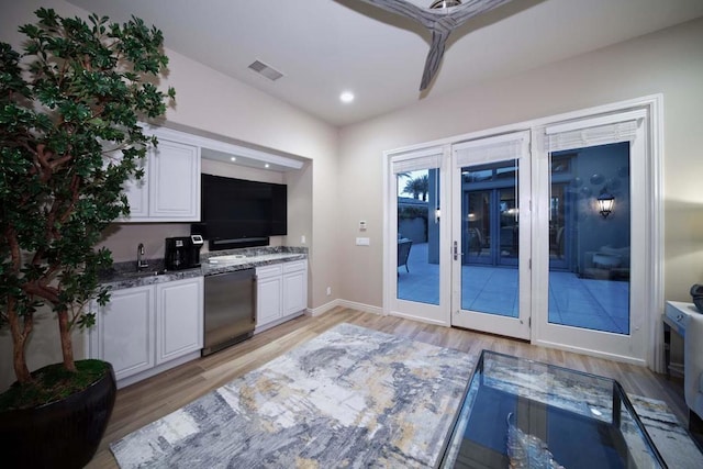 interior space with dishwasher, light hardwood / wood-style floors, white cabinetry, and dark stone counters