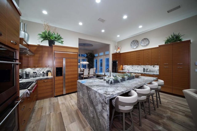 kitchen with a spacious island, a breakfast bar area, tasteful backsplash, wood-type flooring, and stainless steel appliances