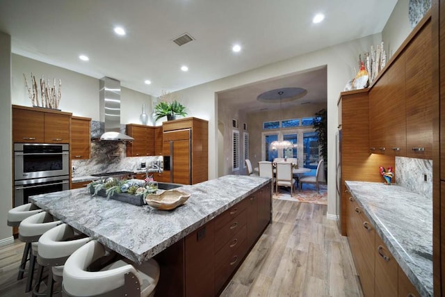 kitchen with a center island, wall chimney range hood, light hardwood / wood-style flooring, double oven, and paneled built in fridge