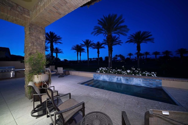 pool at night featuring area for grilling and a patio area