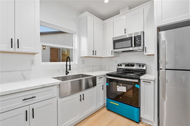 kitchen with light stone countertops, stainless steel appliances, sink, light hardwood / wood-style flooring, and white cabinetry