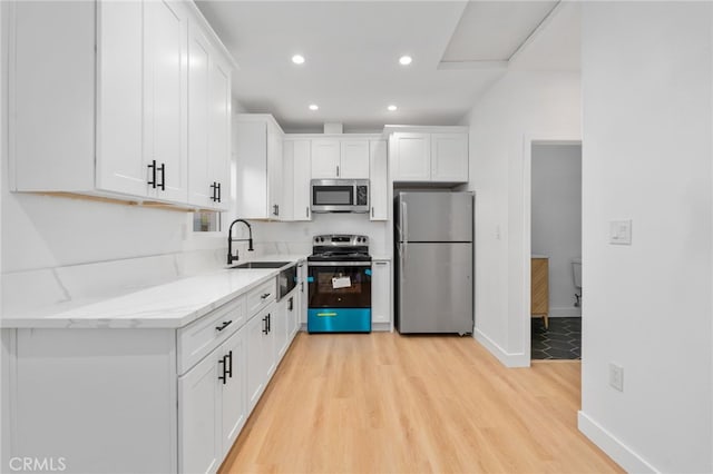 kitchen with light stone counters, stainless steel appliances, sink, light hardwood / wood-style flooring, and white cabinetry