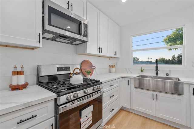 kitchen featuring sink, light hardwood / wood-style floors, light stone counters, white cabinetry, and stainless steel appliances