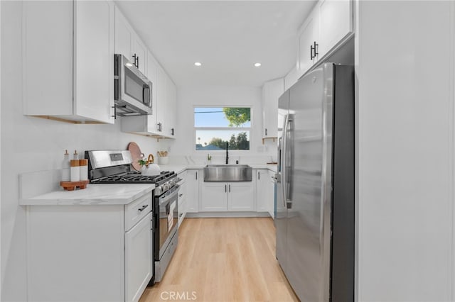 kitchen featuring sink, light hardwood / wood-style flooring, light stone countertops, white cabinetry, and stainless steel appliances