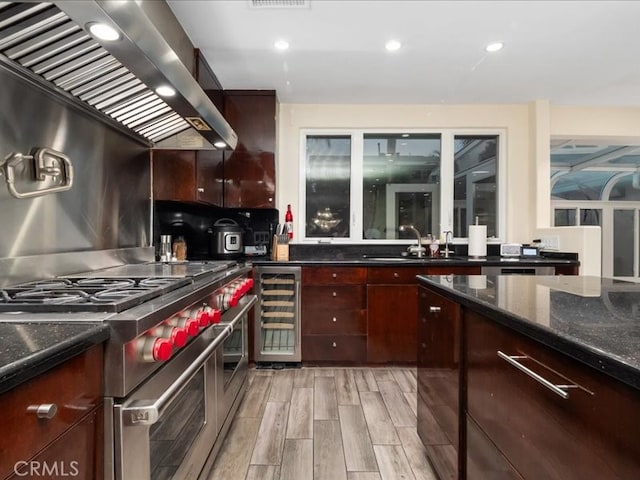 kitchen featuring sink, light wood-type flooring, wall chimney exhaust hood, stainless steel stove, and beverage cooler