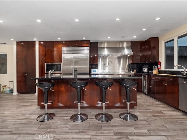 kitchen with built in appliances, wall chimney exhaust hood, a center island, and a breakfast bar area