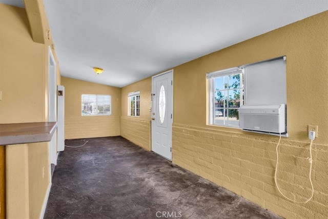 carpeted entrance foyer featuring a wall mounted air conditioner, a healthy amount of sunlight, brick wall, and vaulted ceiling