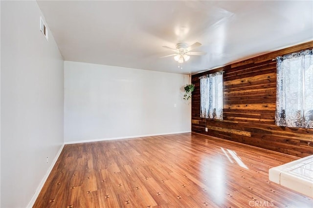 empty room featuring hardwood / wood-style floors, ceiling fan, and wood walls