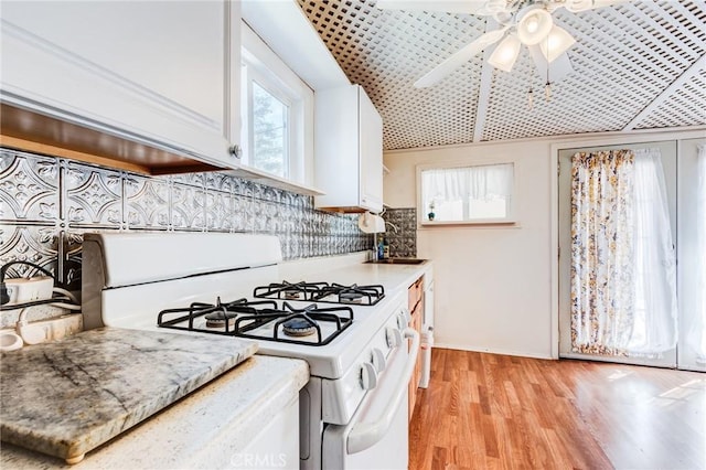 kitchen featuring sink, white cabinetry, tasteful backsplash, light hardwood / wood-style floors, and white gas stove