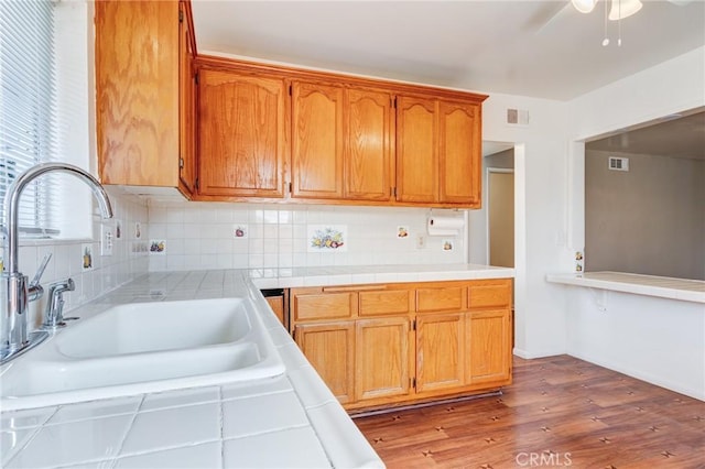 kitchen with tasteful backsplash, sink, tile counters, ceiling fan, and light wood-type flooring