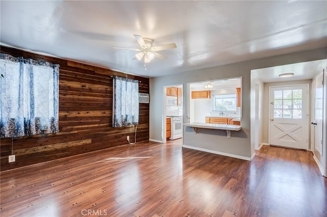 unfurnished living room with ceiling fan, wooden walls, dark hardwood / wood-style floors, and sink