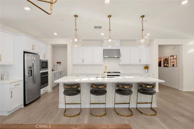 kitchen featuring white cabinets, stainless steel appliances, a kitchen island with sink, and wall chimney range hood