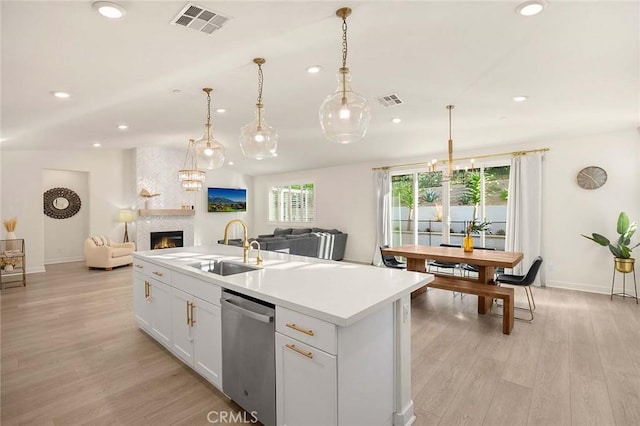 kitchen with stainless steel dishwasher, a healthy amount of sunlight, a center island with sink, and white cabinets