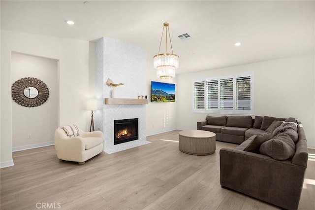 living room featuring a large fireplace, an inviting chandelier, and light hardwood / wood-style flooring