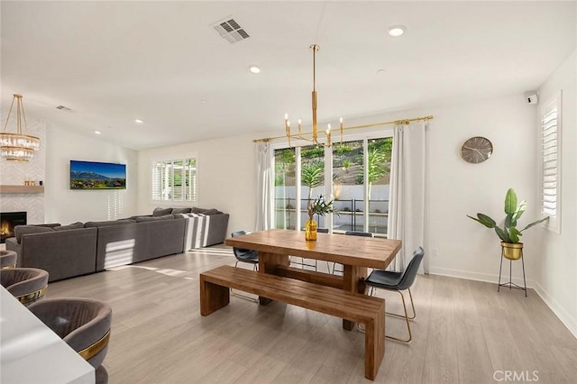 dining room featuring a large fireplace, a chandelier, plenty of natural light, and light hardwood / wood-style floors