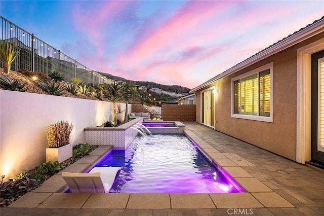 pool at dusk featuring pool water feature and an in ground hot tub