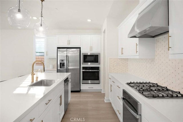 kitchen with appliances with stainless steel finishes, wall chimney exhaust hood, sink, white cabinetry, and hanging light fixtures