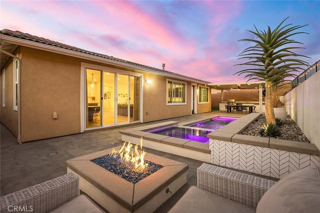 pool at dusk with an in ground hot tub, a patio, an outdoor bar, and an outdoor fire pit