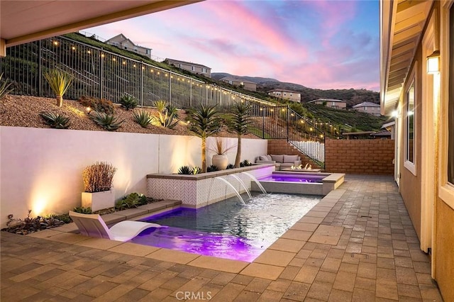 pool at dusk featuring an in ground hot tub and pool water feature