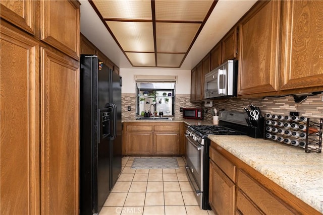 kitchen featuring sink, light stone counters, backsplash, light tile patterned floors, and black appliances