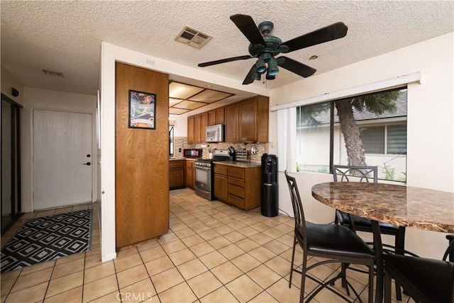 kitchen featuring stainless steel gas stove, ceiling fan, light tile patterned floors, and tasteful backsplash