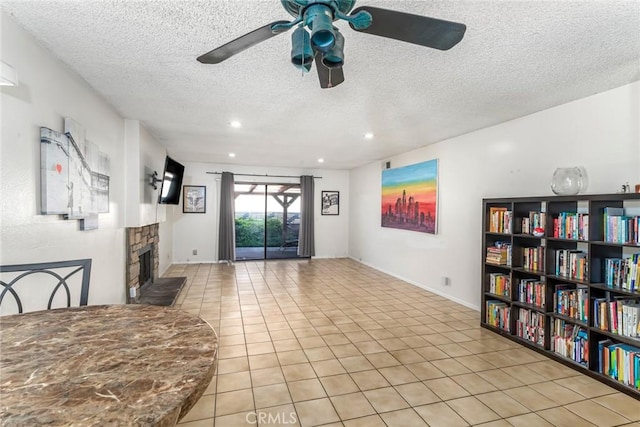 living area with a textured ceiling, a stone fireplace, tile patterned flooring, recessed lighting, and a ceiling fan