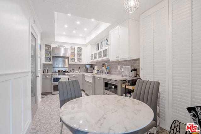 kitchen featuring double oven range, wall chimney exhaust hood, a raised ceiling, white cabinets, and light stone counters