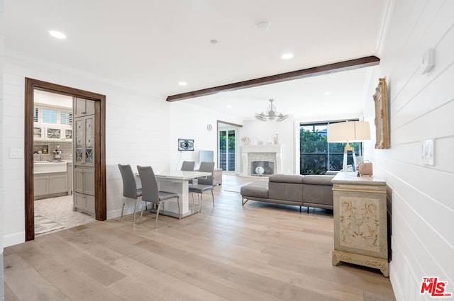 living room featuring beam ceiling, ornamental molding, an inviting chandelier, and light wood-type flooring