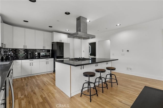 kitchen with appliances with stainless steel finishes, a center island, white cabinetry, island range hood, and light hardwood / wood-style flooring