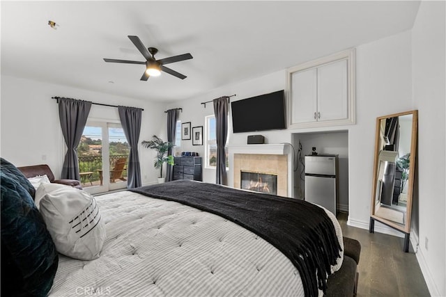 bedroom featuring ceiling fan, wood-type flooring, stainless steel refrigerator, and a tile fireplace